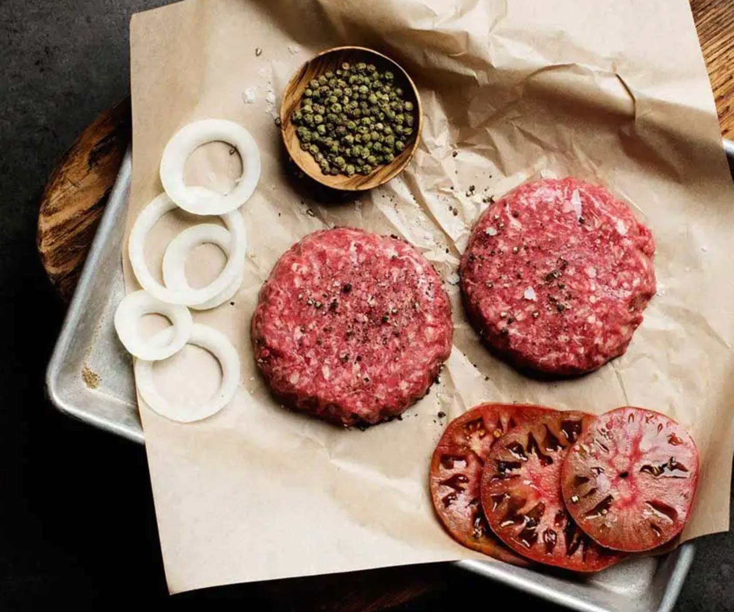 Grass fed burger patties on a tray with onions and tomatoes