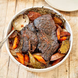 Roasted chuck roast with vegetables in a white bowl on a wooden surface