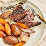 Plated dish of roasted chuck roast with carrots and onions on a beige plate.