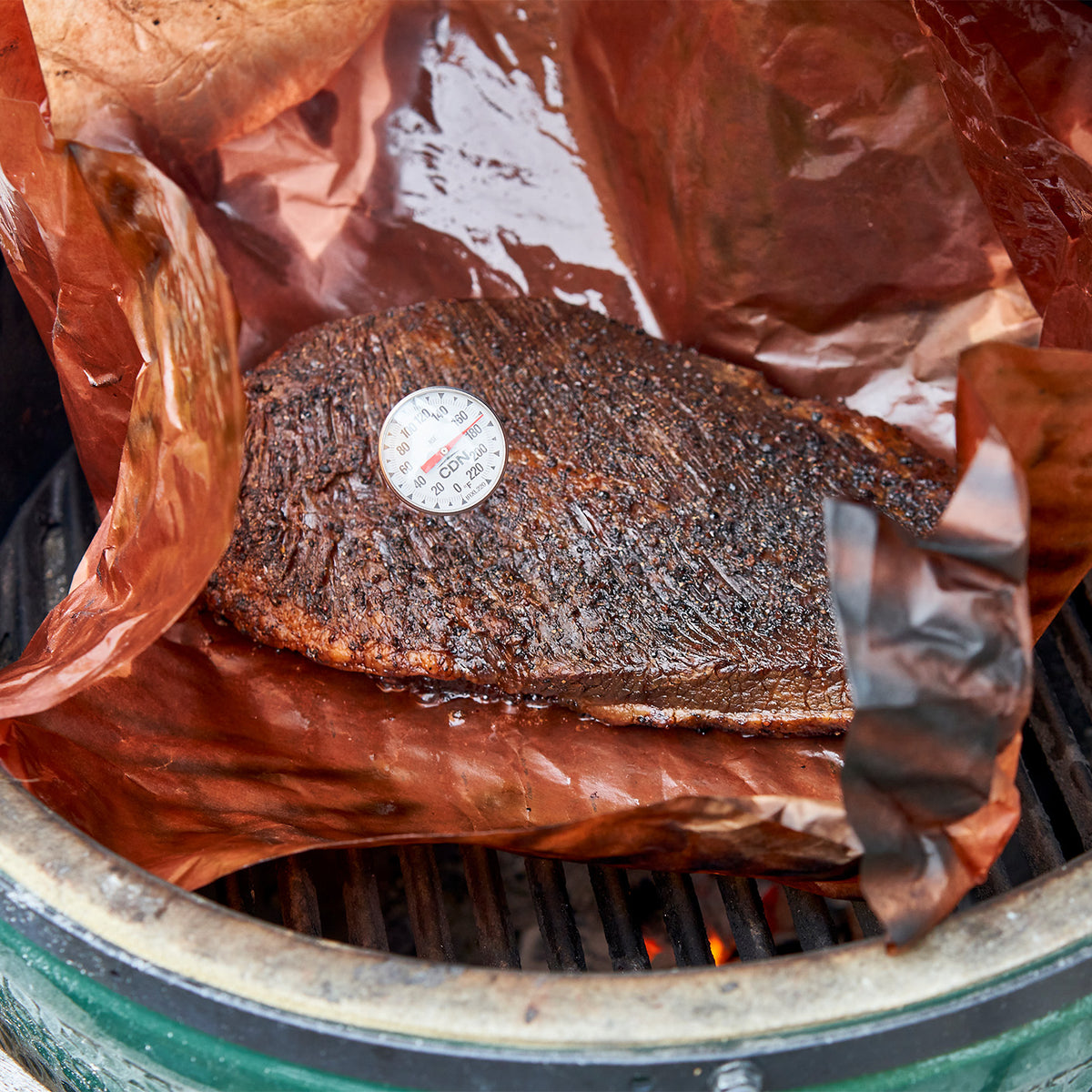 Smoked meat on a grill with a thermometer, wrapped in brown paper.