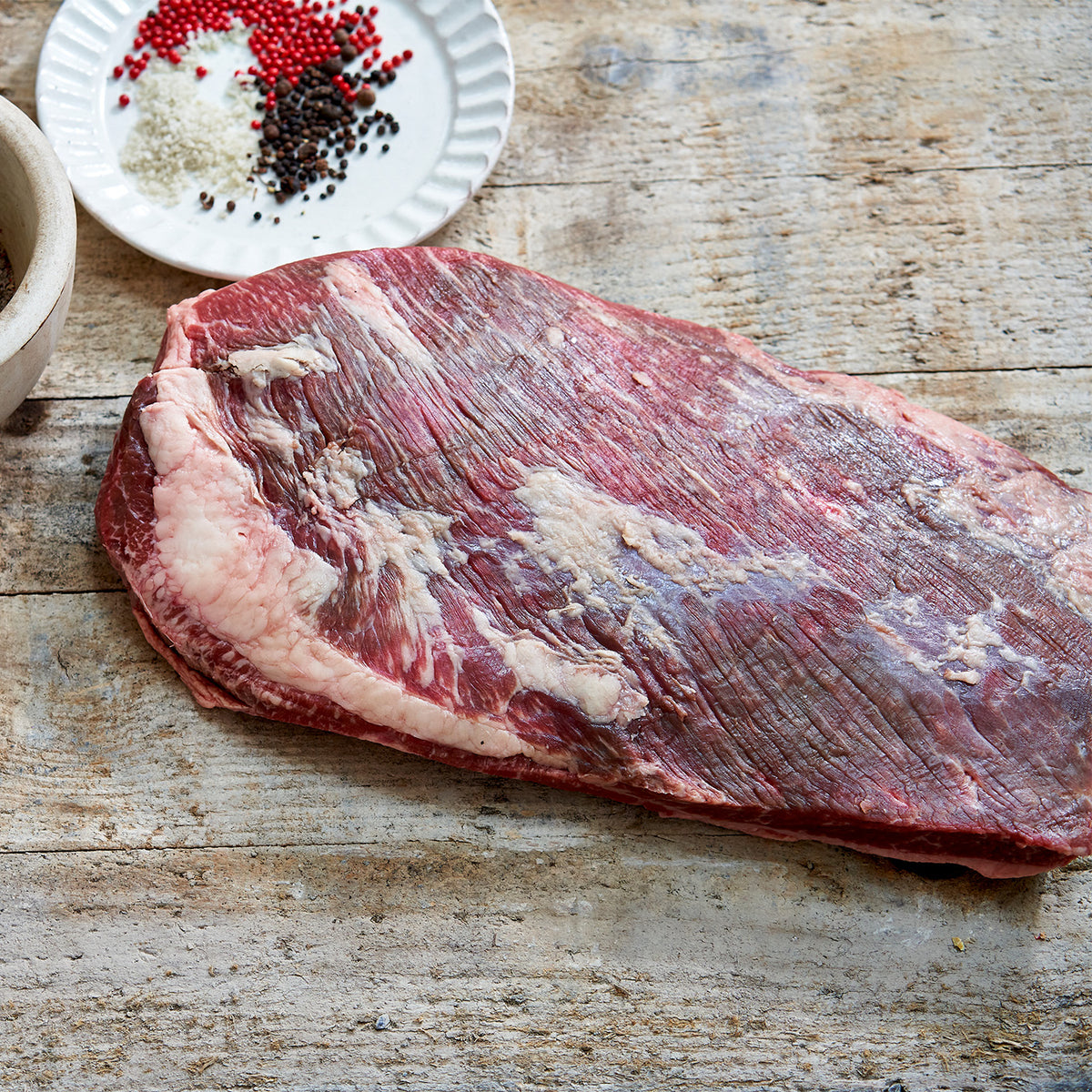 Raw flank steak on a wooden surface with seasonings in the background