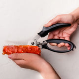 Person using a pair of scissors to cut a piece of sausage on a white background