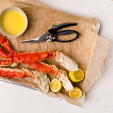 Raw crab legs on brown paper with lemon wedges and a pair of scissors, on a white surface.