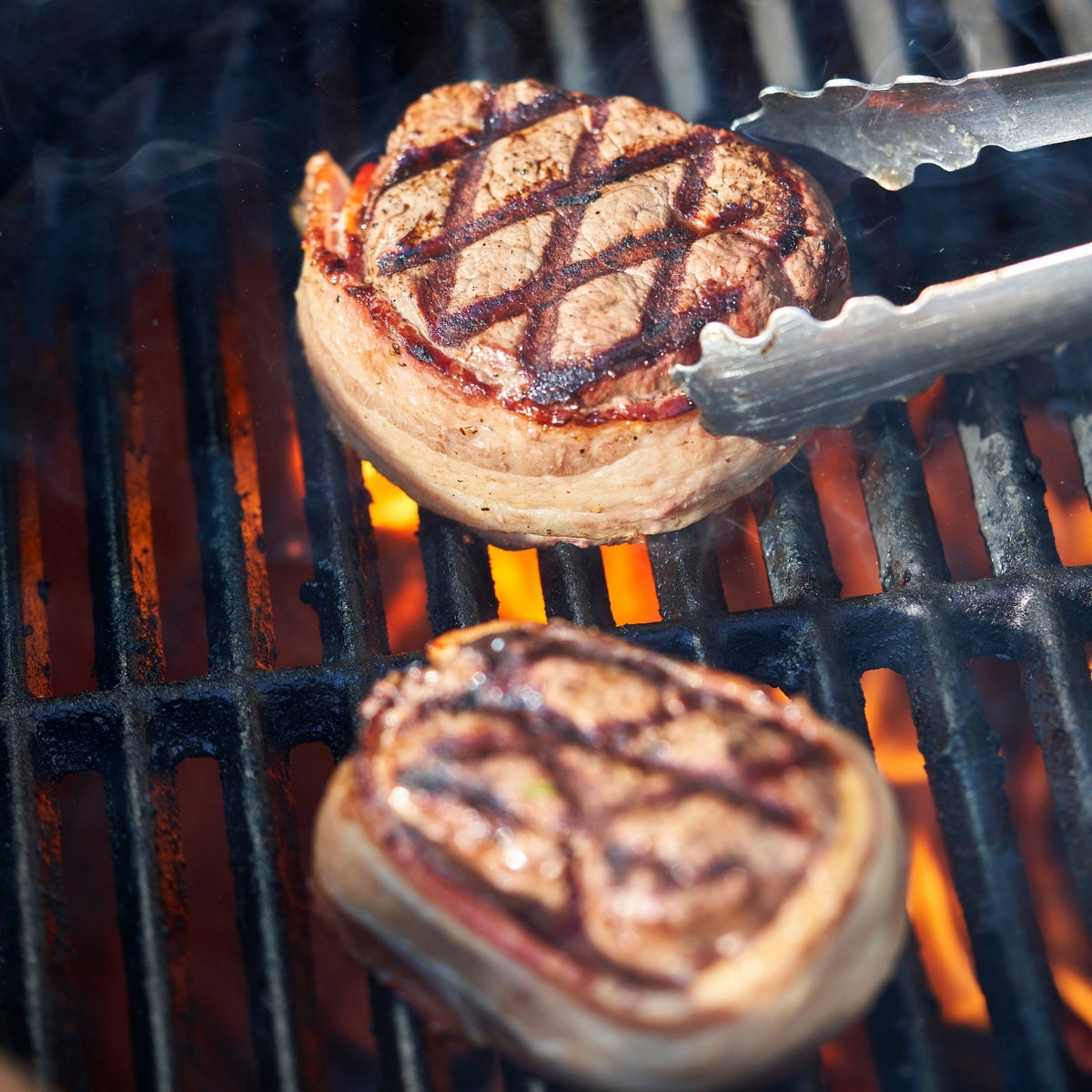 Grilled burger patties on a barbecue with tongs