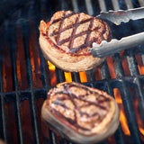 Grilled burger patties on a barbecue with tongs