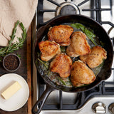 Cooked chicken thighs on cast iron skillet with rosemary and pepper
