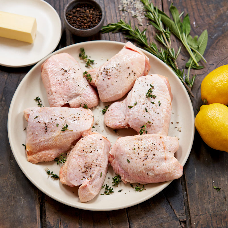 Raw chicken thighs on plate with seasonings on top (Butter, pepper, lemons)