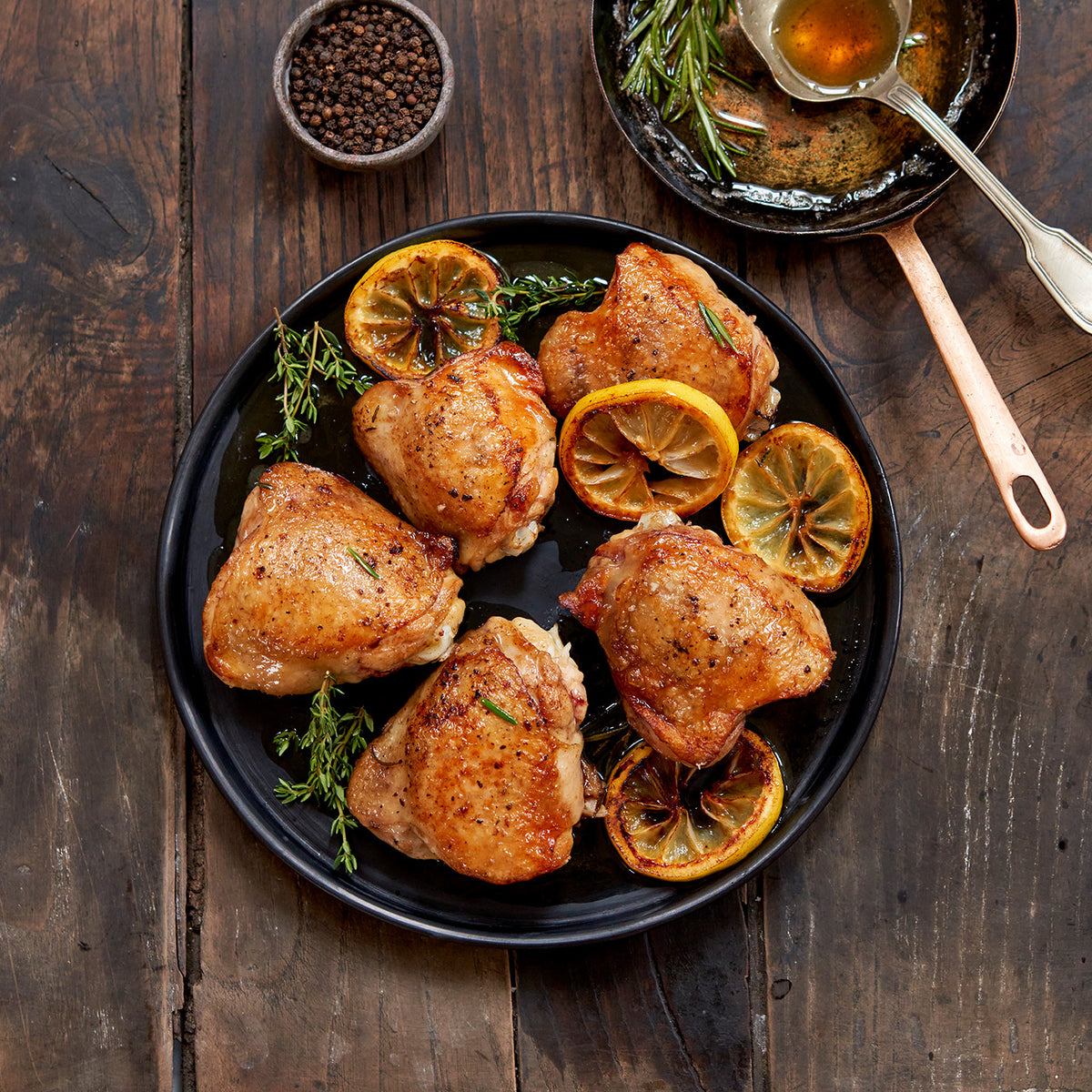 Plated cooked chicken thighs surrounded by rosemary and lemon