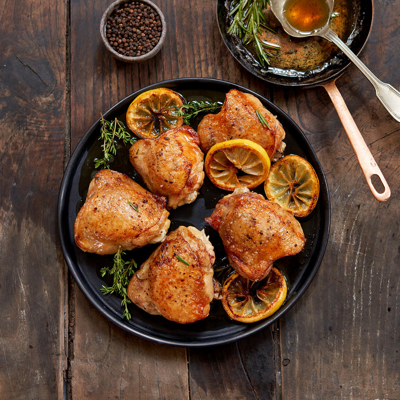 Plated cooked chicken thighs surrounded by rosemary and lemon