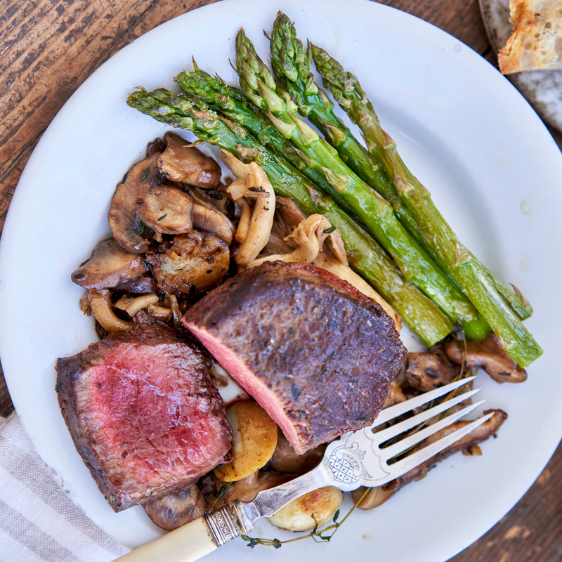 Plated dish of steak, asparagus, and mushrooms on a white plate.