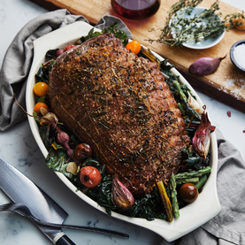 Roasted lamb with vegetables on a white plate, served on a marble table.