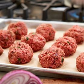 Raw meatballs on a baking tray with a blurred kitchen background