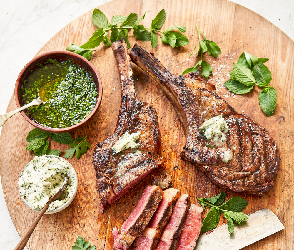 Grilled meat with herbs and a bowl of green sauce on a wooden board