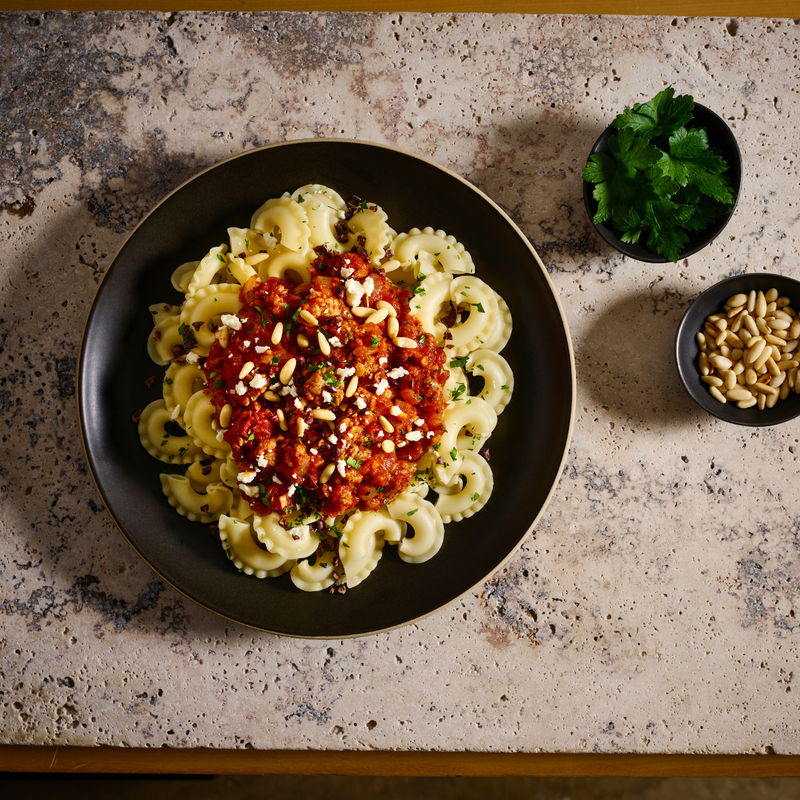 Pasta dish with red sauce and toppings on a textured surface