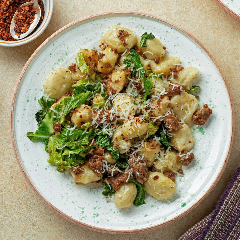 Plate of gnocchi with greens and sausage on a speckled plate