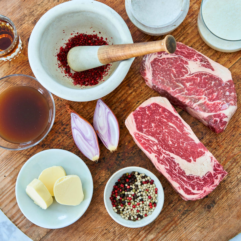 Raw steaks with spices, butter, and onions on a wooden surface