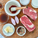 Raw steaks with spices, butter, and onions on a wooden surface