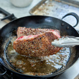 Steak being seared in a cast iron skillet with tongs