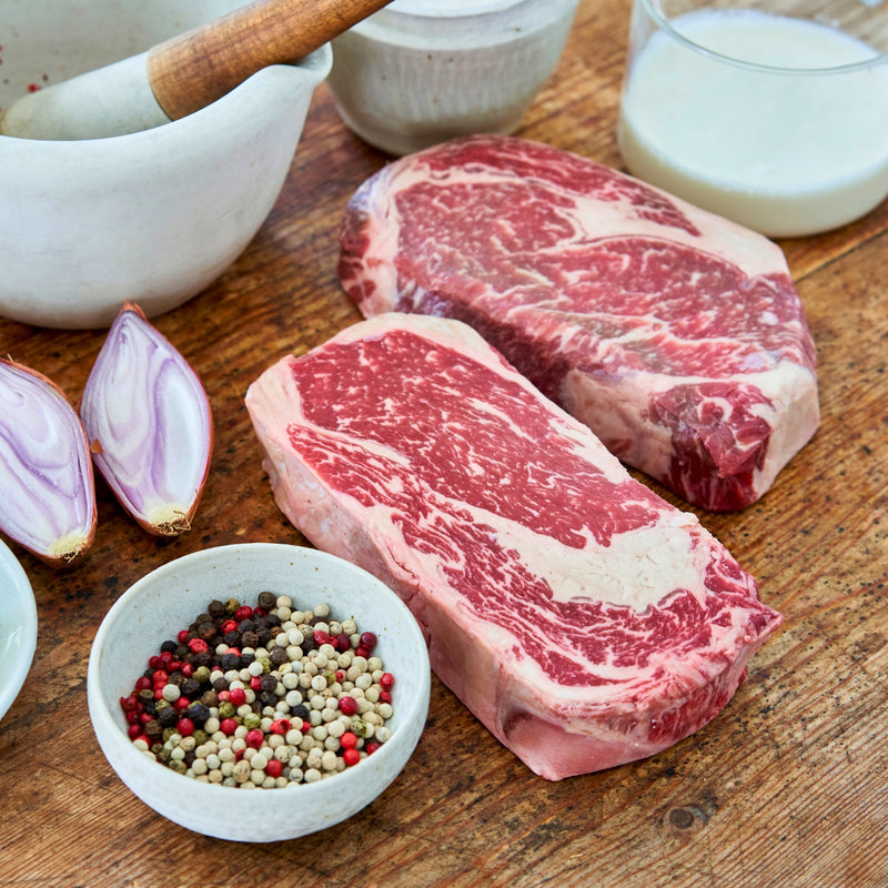 Raw beef steaks on a wooden surface with spices and onions.