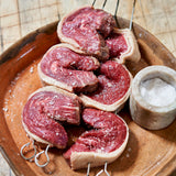 Raw beef slices on skewers with a container of salt on a wooden plate.