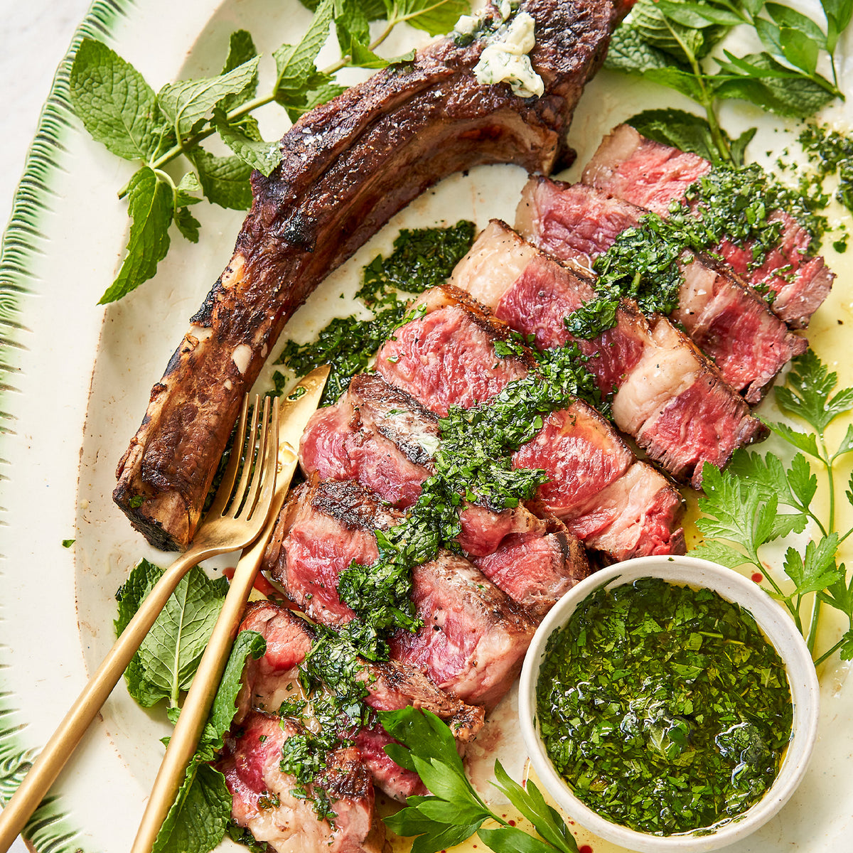 Grilled steak with chimichurri sauce on a plate with herbs and a gold fork.