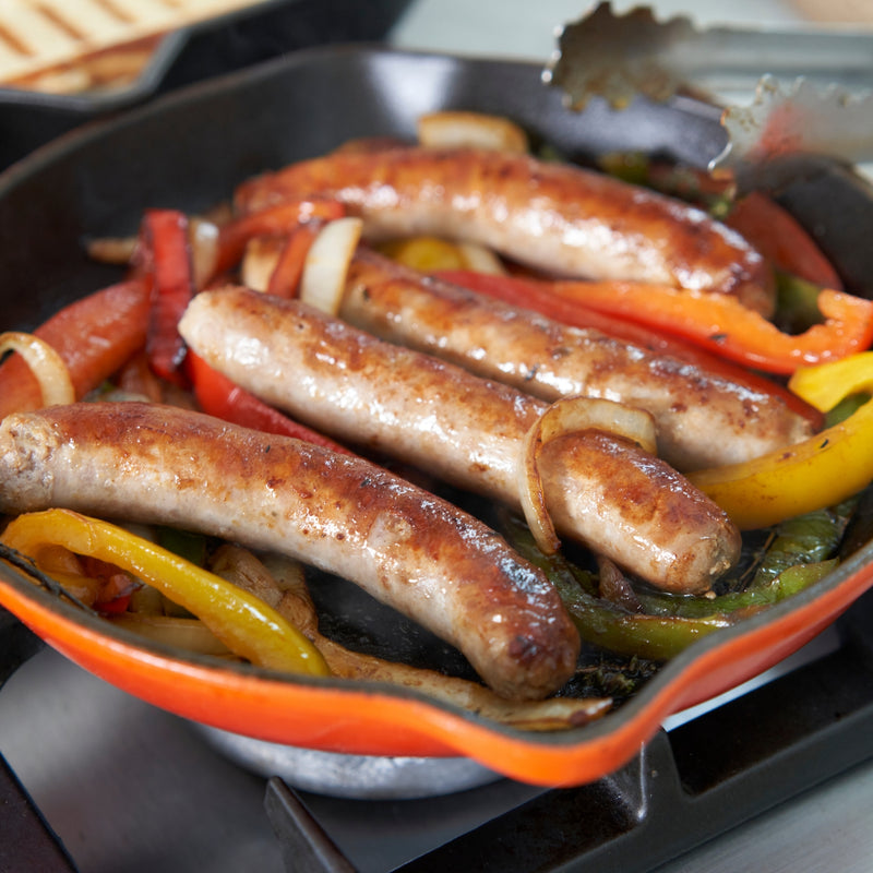 Sausages and vegetables cooking in a skillet on a stove
