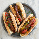 Three hot dogs with sausages, peppers, and onions in buns on a gray plate.