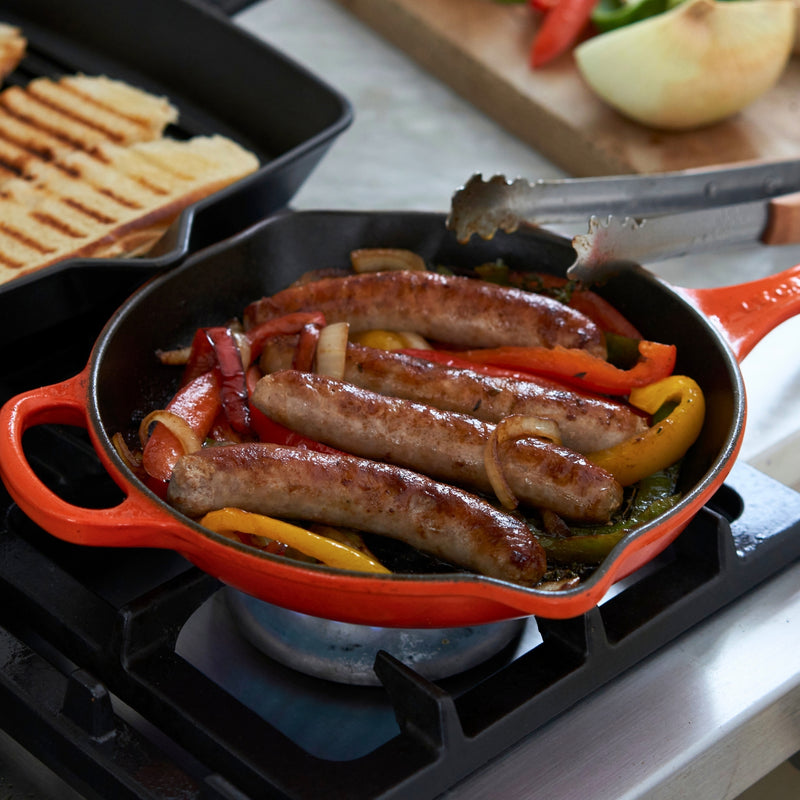Sausages and vegetables being cooked in a red skillet on a stove.