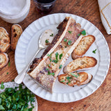 Plated dish of osso buco with bread slices on a wooden table