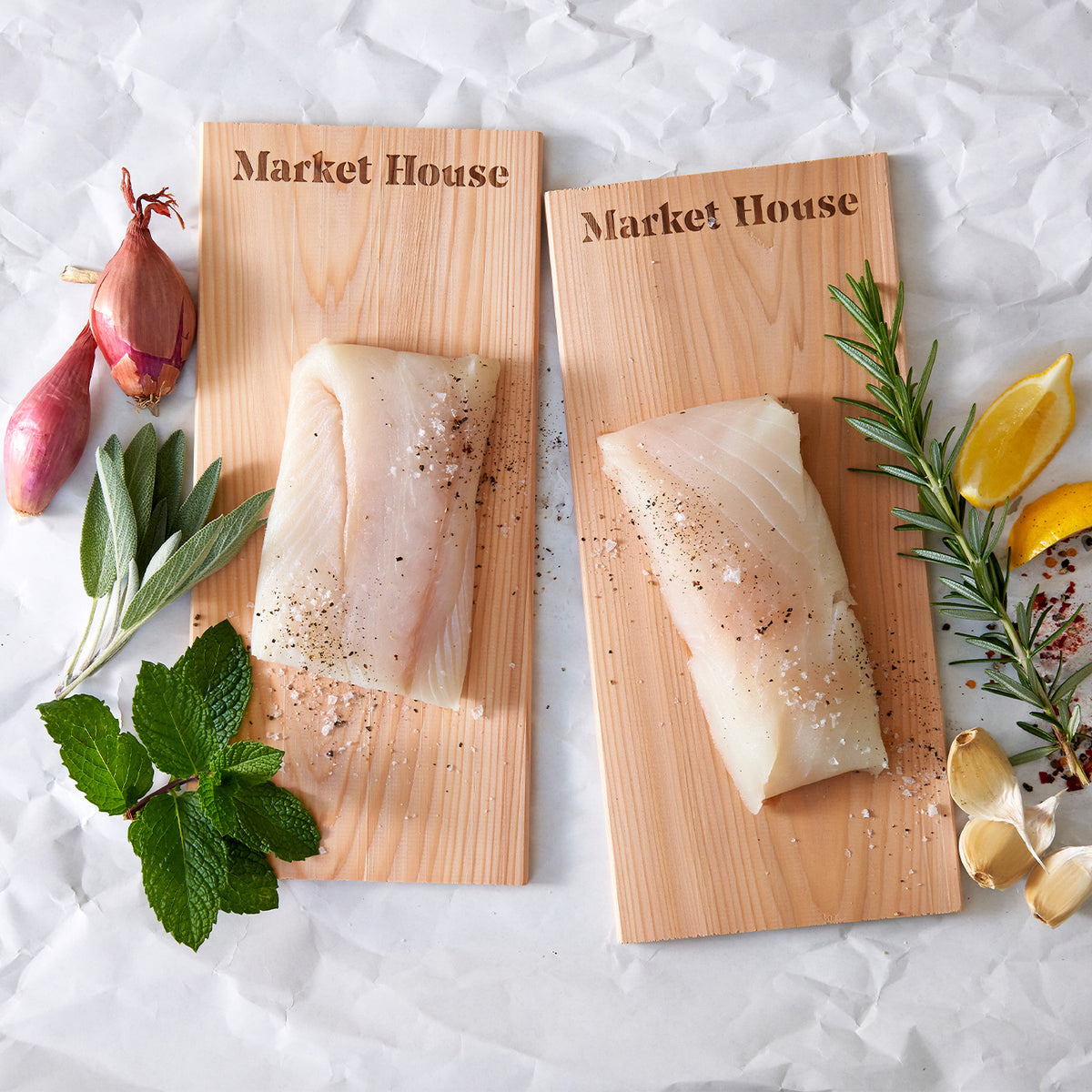 Two pieces of fish on wooden cedar planks with herbs and spices on a textured surface.
