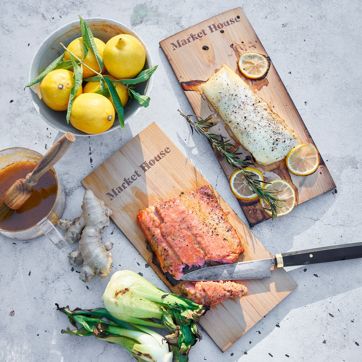 Salmon fillets on wooden cedar planks with lemons and herbs on a light gray surface.