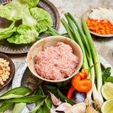 Assorted ingredients including ground chicken, vegetables, and herbs on a stone surface.