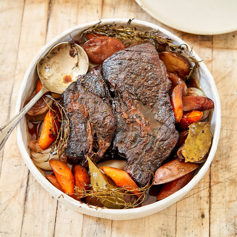Roasted chuck roast with vegetables in a white bowl on a wooden surface