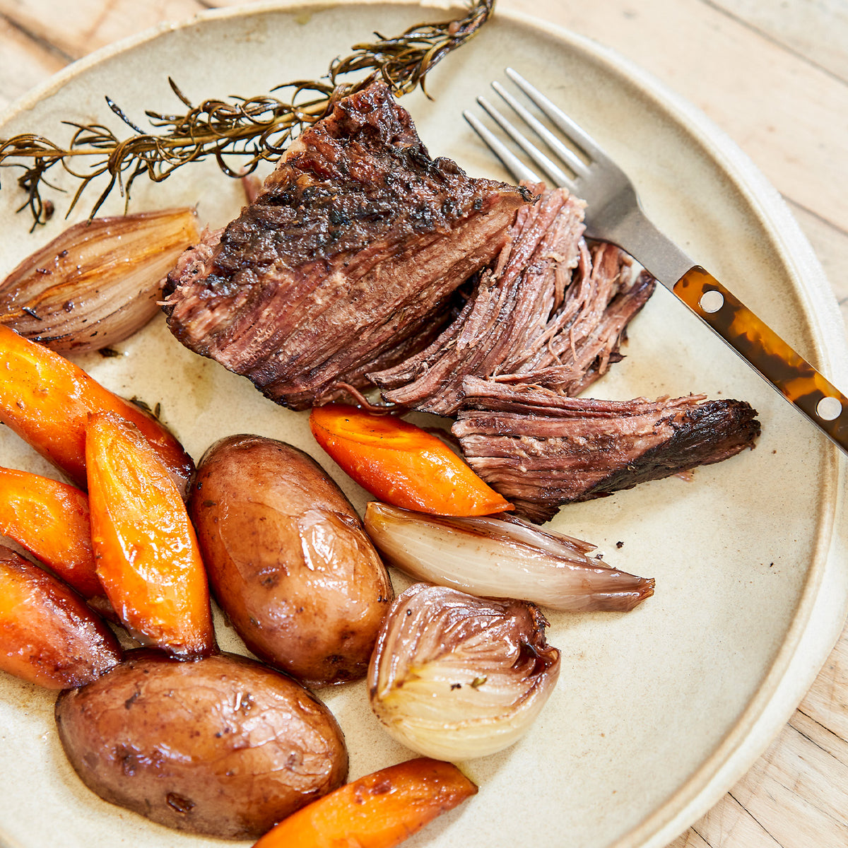 Plated dish of roasted chuck roast with carrots and onions on a beige plate.
