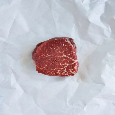 A single raw beef cut with visible marbling, placed on crumpled white paper.