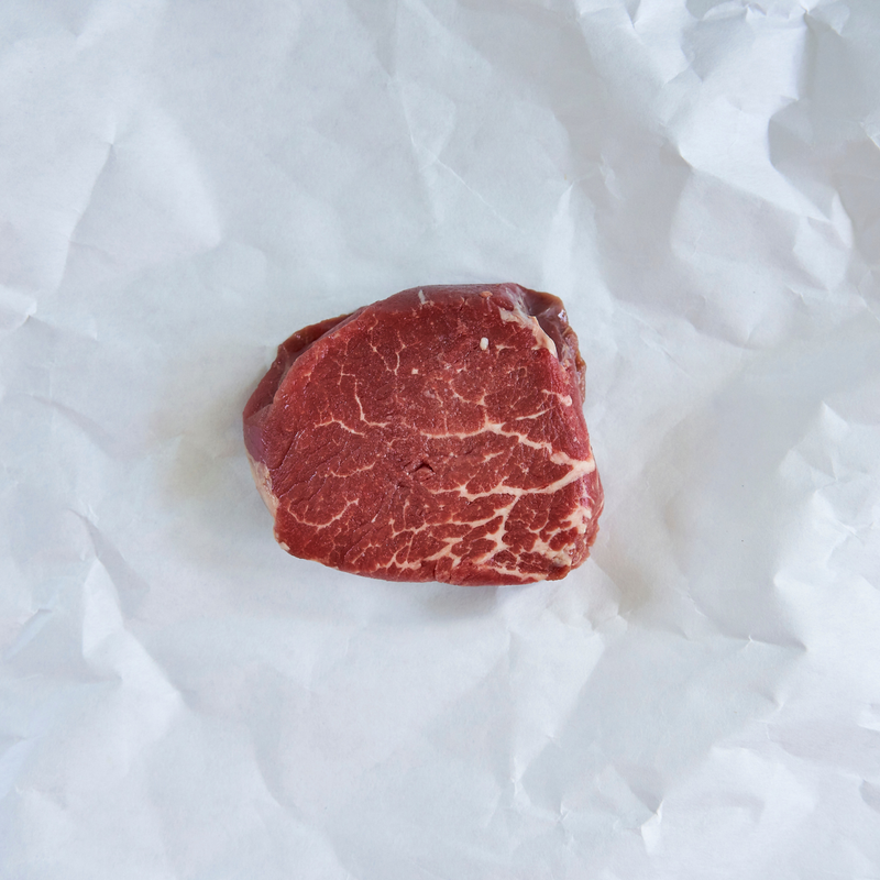 A single raw beef cut with visible marbling, placed on crumpled white paper.