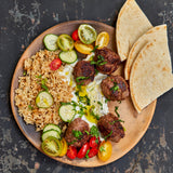 Plated dish with lamb meatballs, rice, vegetables, and flatbread on a dark surface