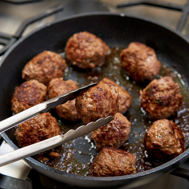 Meatballs cooking in a pan with tongs