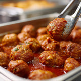 Baked meatballs in a baking dish with a spoon lifting one out.