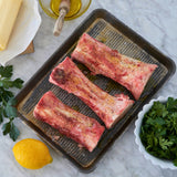 Raw ribs on a baking tray with lemon and herbs on a marble surface