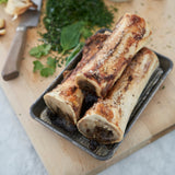 Roasted bone marrow on a tray with herbs on a wooden board