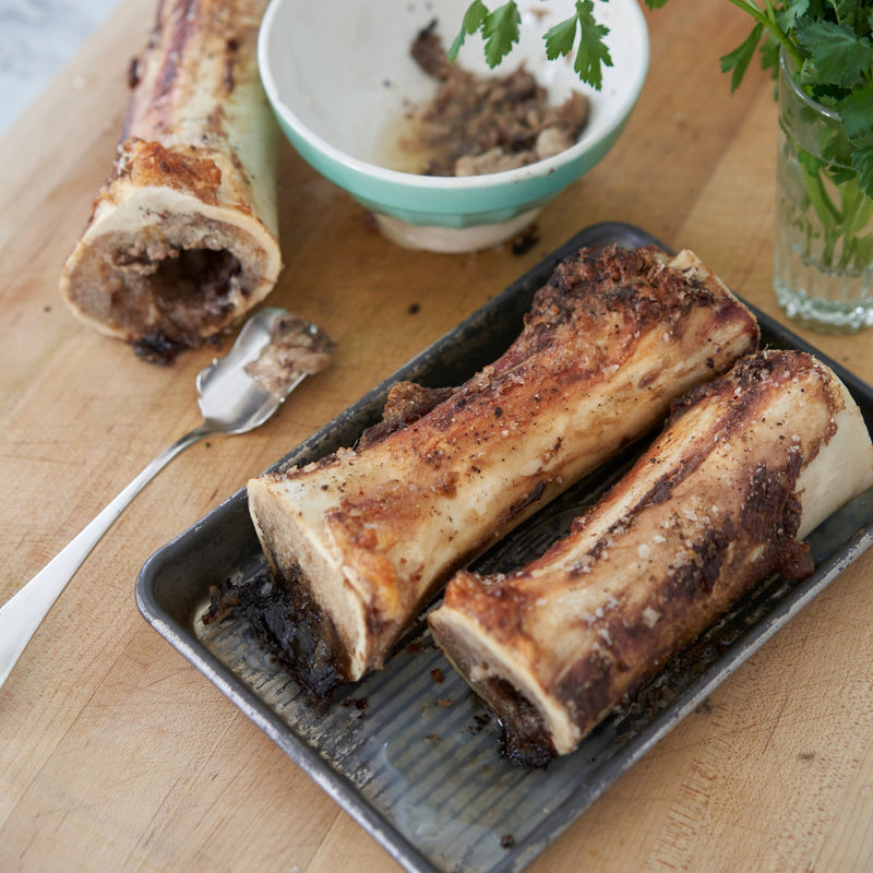Roasted bones on a tray with a bowl of herbs on a wooden surface