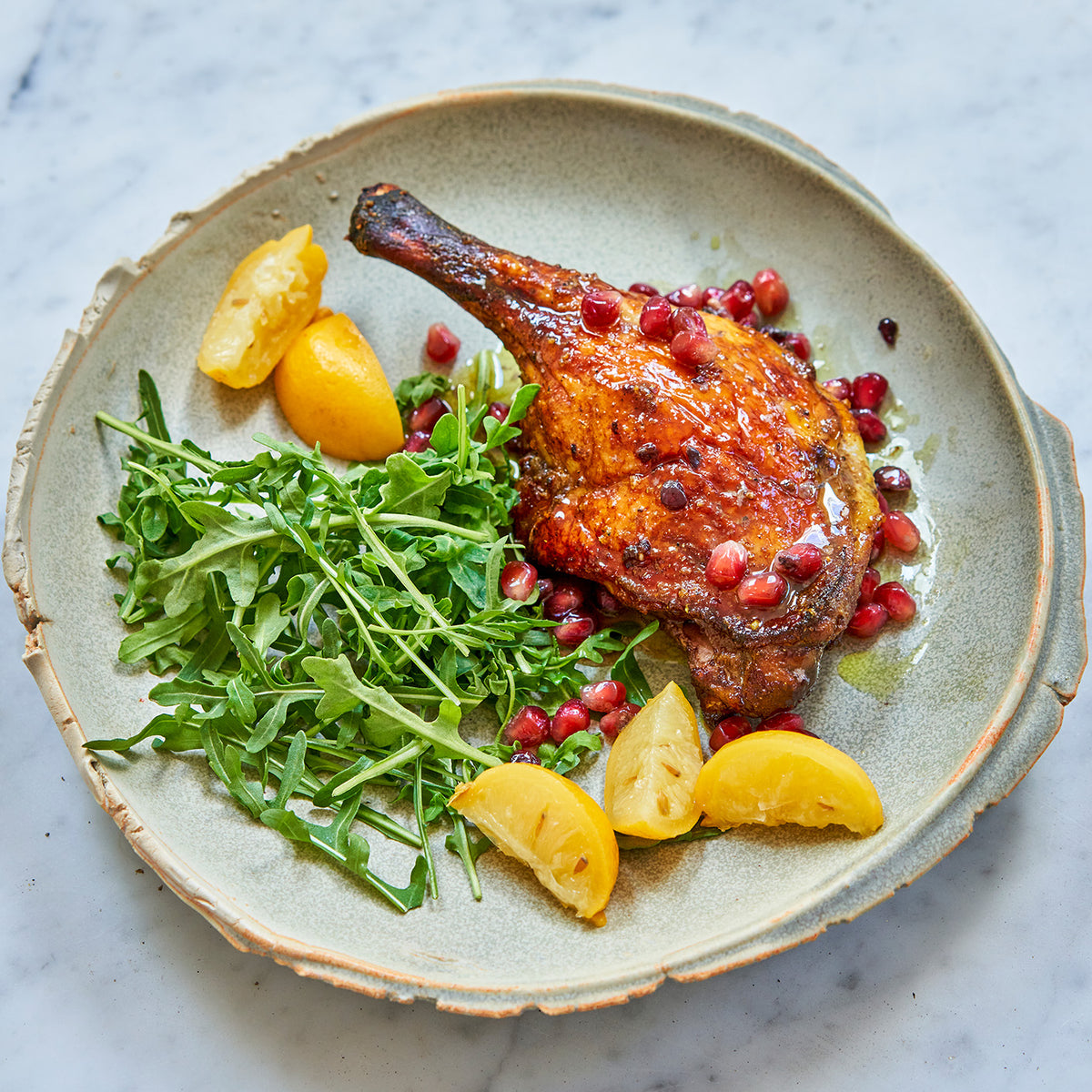 Cooked Moulard deck leg quarters, arugula, lemon, and pomegranate seeds served on a plate 