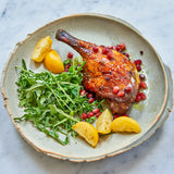 Cooked Moulard deck leg quarters, arugula, lemon, and pomegranate seeds served on a plate 