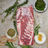 Raw Boneless, Skin-On Whole Pork Belly with herbs and spices on a stone surface