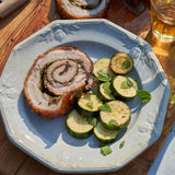 Sliced pork roll with zucchini on a white plate on a wooden table