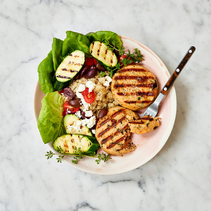 Plated dish with grilled salmon patties, quinoa, vegetables, and a fork on a marble background