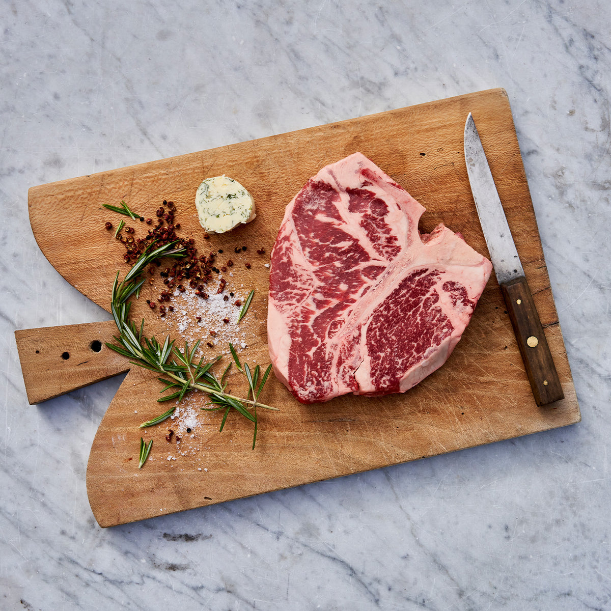 Raw steak on a wooden cutting board with herbs and spices, on a marble surface.