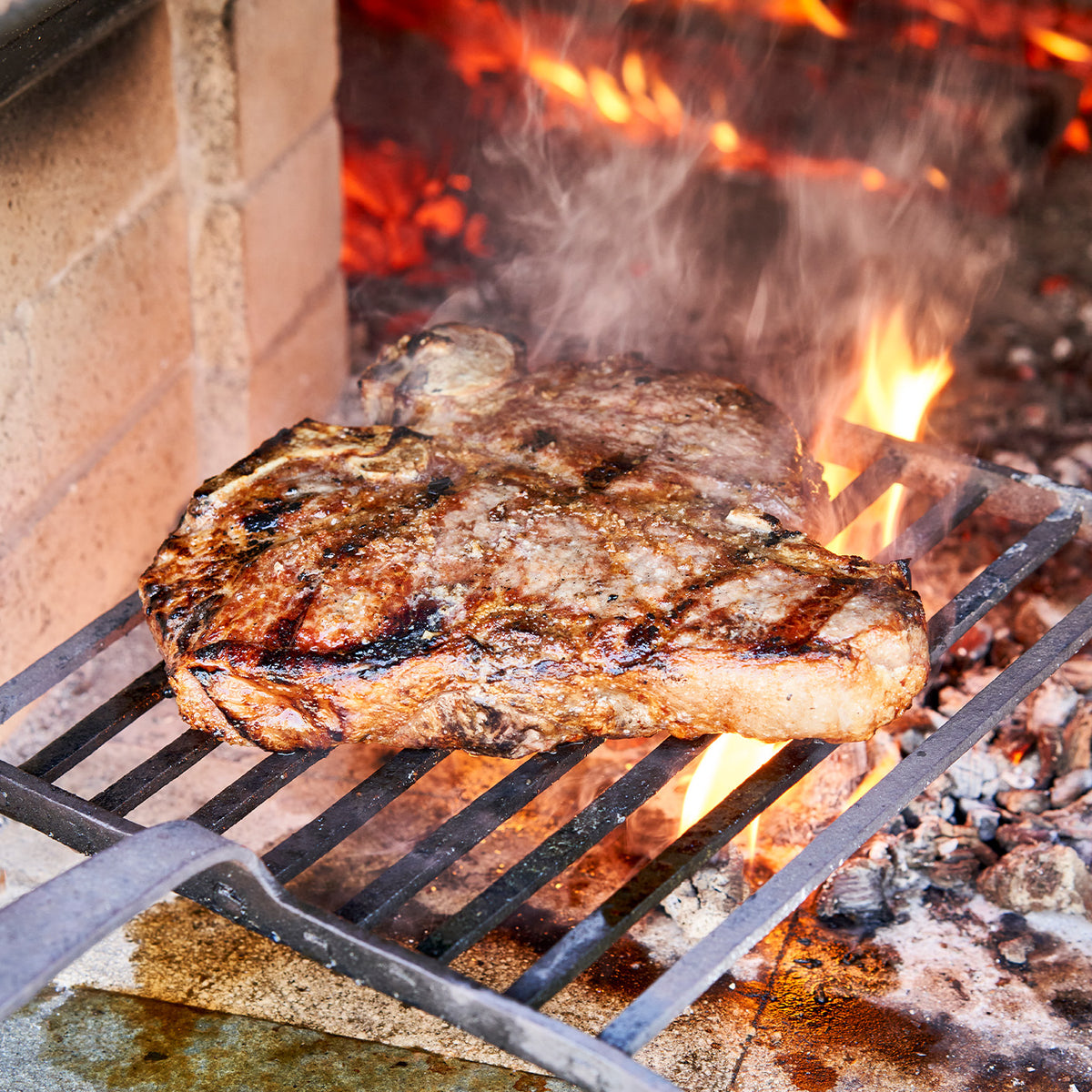 Steak being grilled over an open flame on a barbecue.