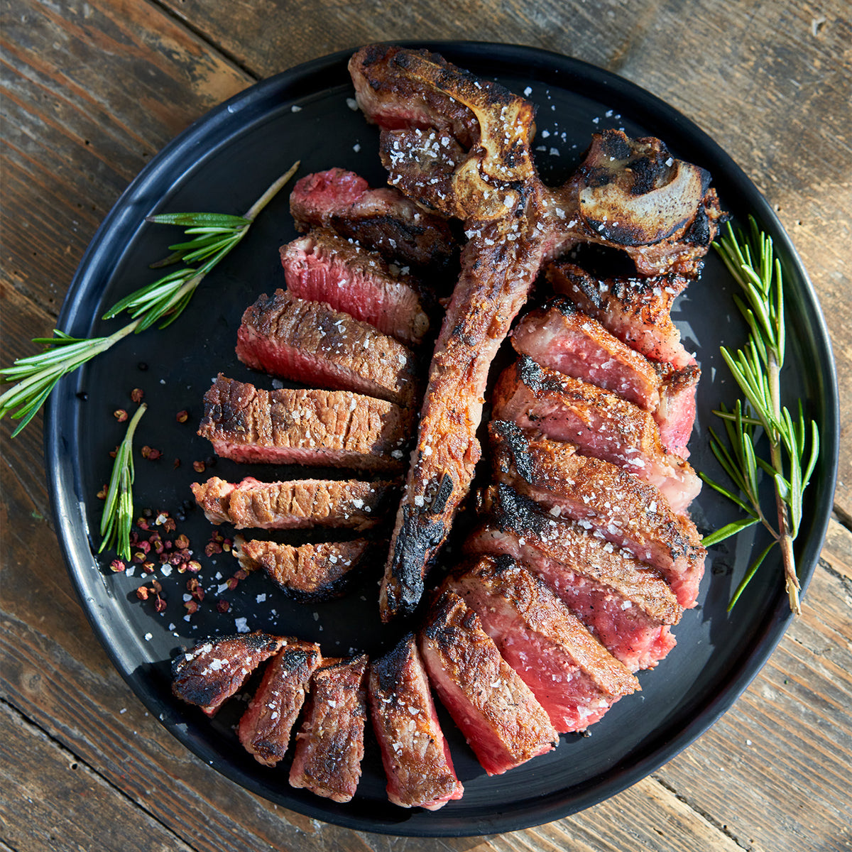 Grilled steak on a black plate with rosemary on a wooden surface